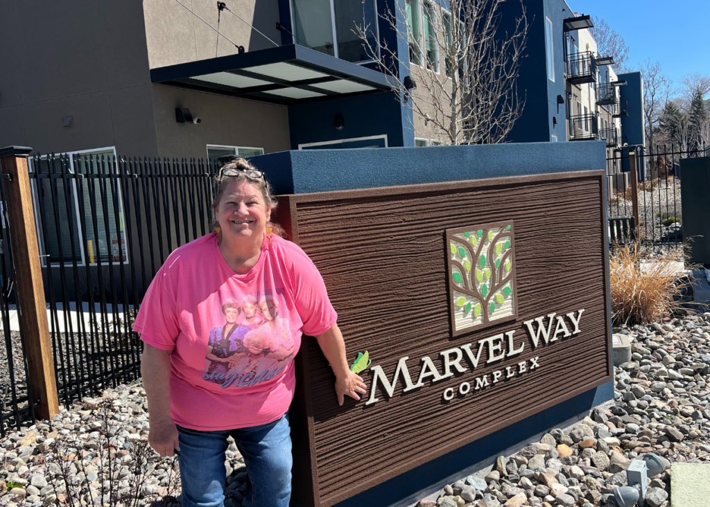 linda buzick wearing pink shirt standing in front of marvel way sober living apartments